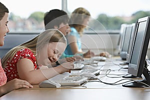 Girl (10-12) with Down syndrome using computer in computer lab children in background photo