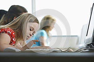 Girl (10-12) with Down syndrome using computer in computer lab children in background photo