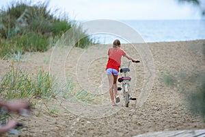 Girl drags a bicycle on the sand at the seaside