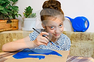 A girl drawing blue gouache cardboard, artistic creation at home, makes creative artwork