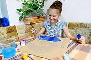 A girl drawing blue gouache cardboard, artistic creation at home, makes creative artwork