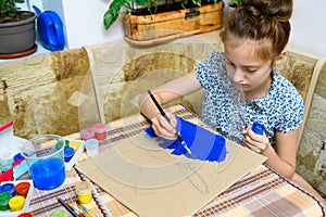 A girl drawing blue gouache cardboard, artistic creation at home, makes creative artwork