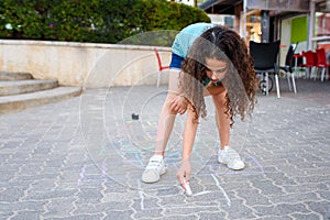 Girl drawing hopscotch with chalk on playground.