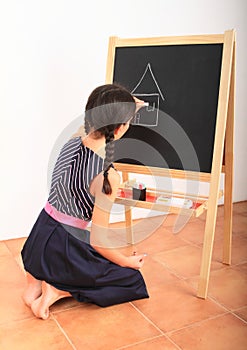 Girl drawing house on black blackboard