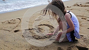 Girl drawing and jumps on a sand beach.