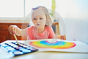 Girl drawing rainbow with colorful aquarelle paints