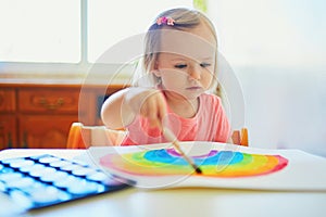 Girl drawing rainbow with colorful aquarelle paints