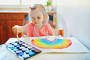 Girl drawing rainbow with colorful aquarelle paints