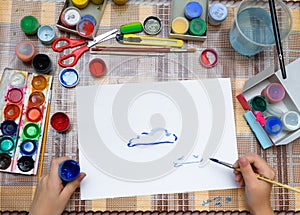 A girl drawing watercolor blue clouds on a blank white paper, artistic creation at home, makes creative artwork