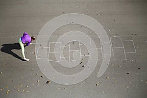 Girl draws by chalk hopscotch on asphalt at autumn photo