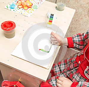 A girl draws a drawing with paints on a sheet