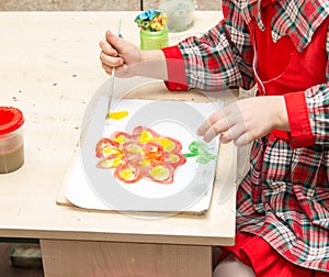 A girl draws a drawing with paints on a sheet