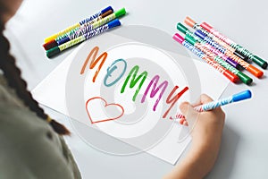 a girl draws a gift for her mother for Mother\'s Day, a multi-colored inscription with felt-tip pens mommy