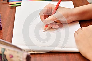 The girl draws a heart with colored pencils on a white sheet of paper