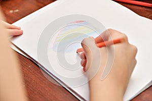 The girl draws a heart with colored pencils on a white sheet of paper