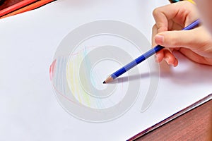 The girl draws a heart with colored pencils on a white sheet of paper