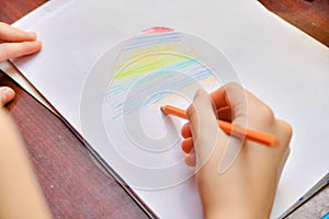 The girl draws a heart on a white sheet of paper and paints it in the form of a rainbow with colored pencils