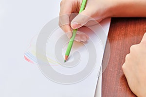 The girl draws a heart on a white sheet of paper and paints it in the form of a rainbow with colored pencils