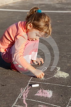 Girl draws painting line house a chalk on asphalt