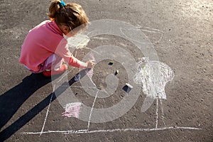 Girl draws painting sun house chalk on asphalt