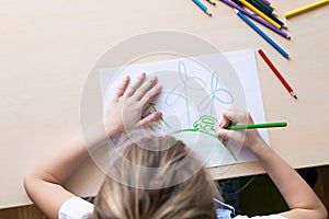 A girl draws with pencils a green house planet car wind power plants. Concept of ecology and environmental protection.