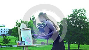 Girl draws on plein air on green grass in city park