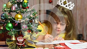The girl draws at the table Christmas pattern, focusing on fur-tree in front of her
