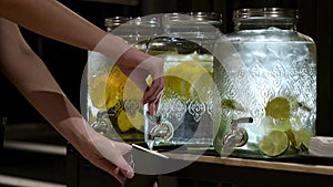 Girl draws water into a glass. lemonade. water with lemon, mint and orange. detox