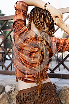 a girl with a dreadlocked hairstyle poses in summer outdoor, bright sunlight, dressed in a plaid shirt and shorts