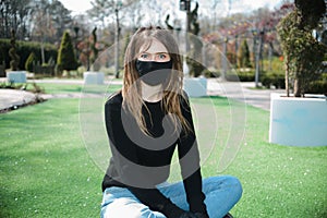 Girl with dreadlocks in a black protective mask from coronavirus with eyes wide open in a park on a green meadow