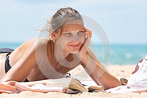 Girl dreamily looks into the distance lying on a sandy beach by the sea with a book