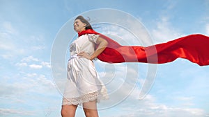 Girl dreams of becoming a superhero. sexy superhero girl standing on the field in a red cloak, cloak fluttering in the