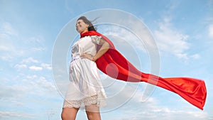 Girl dreams of becoming a superhero. sexy superhero girl standing on the field in a red cloak, cloak fluttering in the