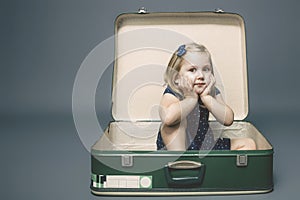 Girl with dreamy expression sitting inside a vintage suitcase