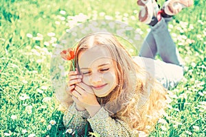 Girl on dreamy face holds red tulip flower, enjoy aroma. Spring break concept. Child enjoy spring sunny day while lying