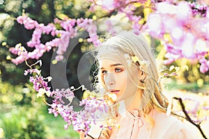 Girl on dreamy face, tender blonde near violet flowers of judas tree, nature background. Young woman enjoy flowers in