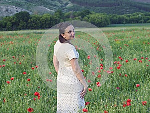 A girl in a dress on the background of a poppy field poses