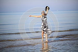 Girl in a dress in flowers frolics by the water on a clear sunny