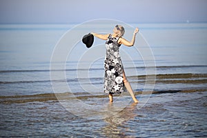 Girl in a dress in flowers frolics by the water on a clear sunny