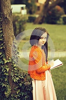 Girl in dress with notebook and pen near tree