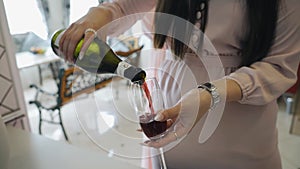 A girl in a dress pours wine into a glass of champagne. Shooting at a party.