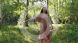 A girl in a dress runs along a forest path. The girl smiles and looks at the camera.