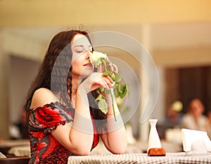 Girl in dress sitting at table in restaurant and enjoy aroma of roses flower waiting a date