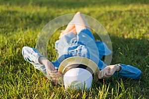 Girl in dress and straw hat lies on the green grass. View from above