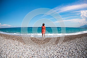 A girl in a dress walks along the beach and looks at the sea