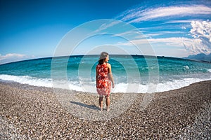 A girl in a dress walks along the beach and looks at the sea