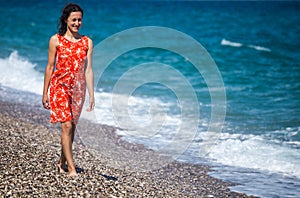 A girl in a dress walks along the beach and looks at the sea