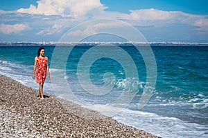 A girl in a dress walks along the beach and looks at the sea