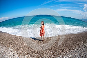 A girl in a dress walks along the beach and looks at the sea