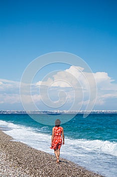 A girl in a dress walks along the beach and looks at the sea